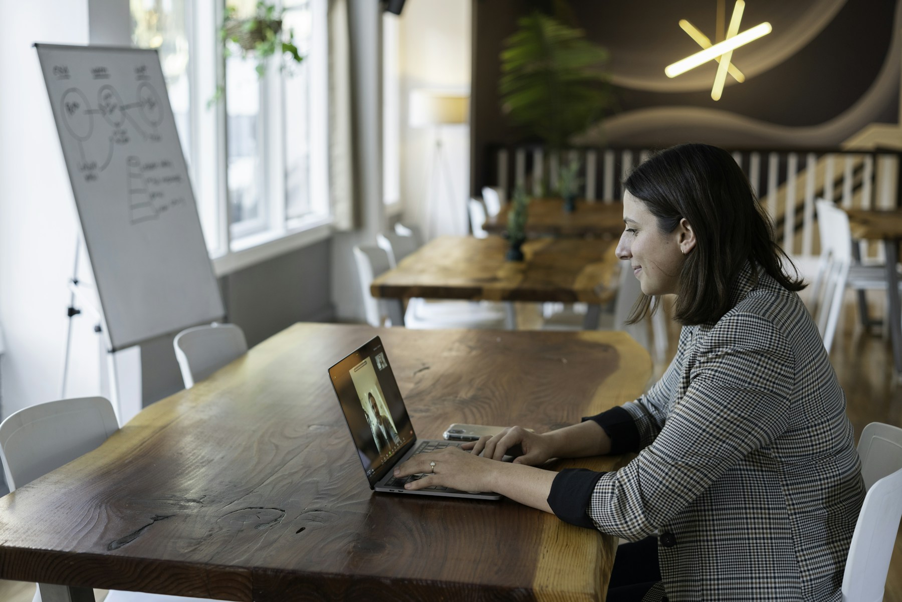 A woman seated at a table using a laptop for a video call.
